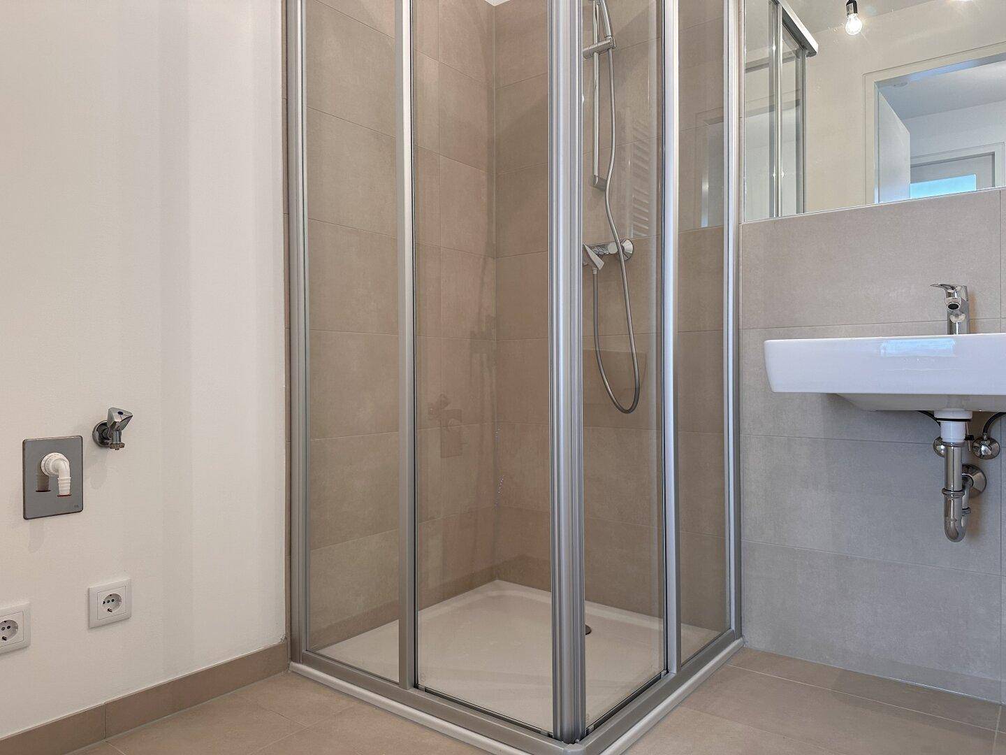 Helles Badezimmer mit moderner Duschkabine und Einzelwaschbecken, ausgestattet mit beigen Fliesen.