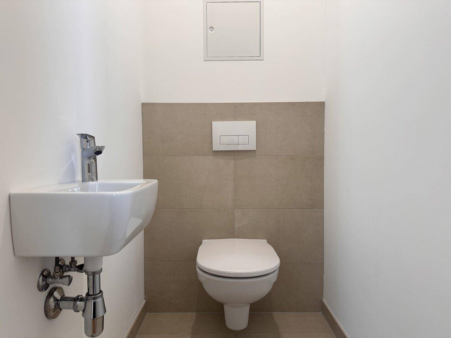 Modernes Gäste-WC mit wandhängender Toilette und kleinem Waschbecken, in neutralen Farben gehalten.