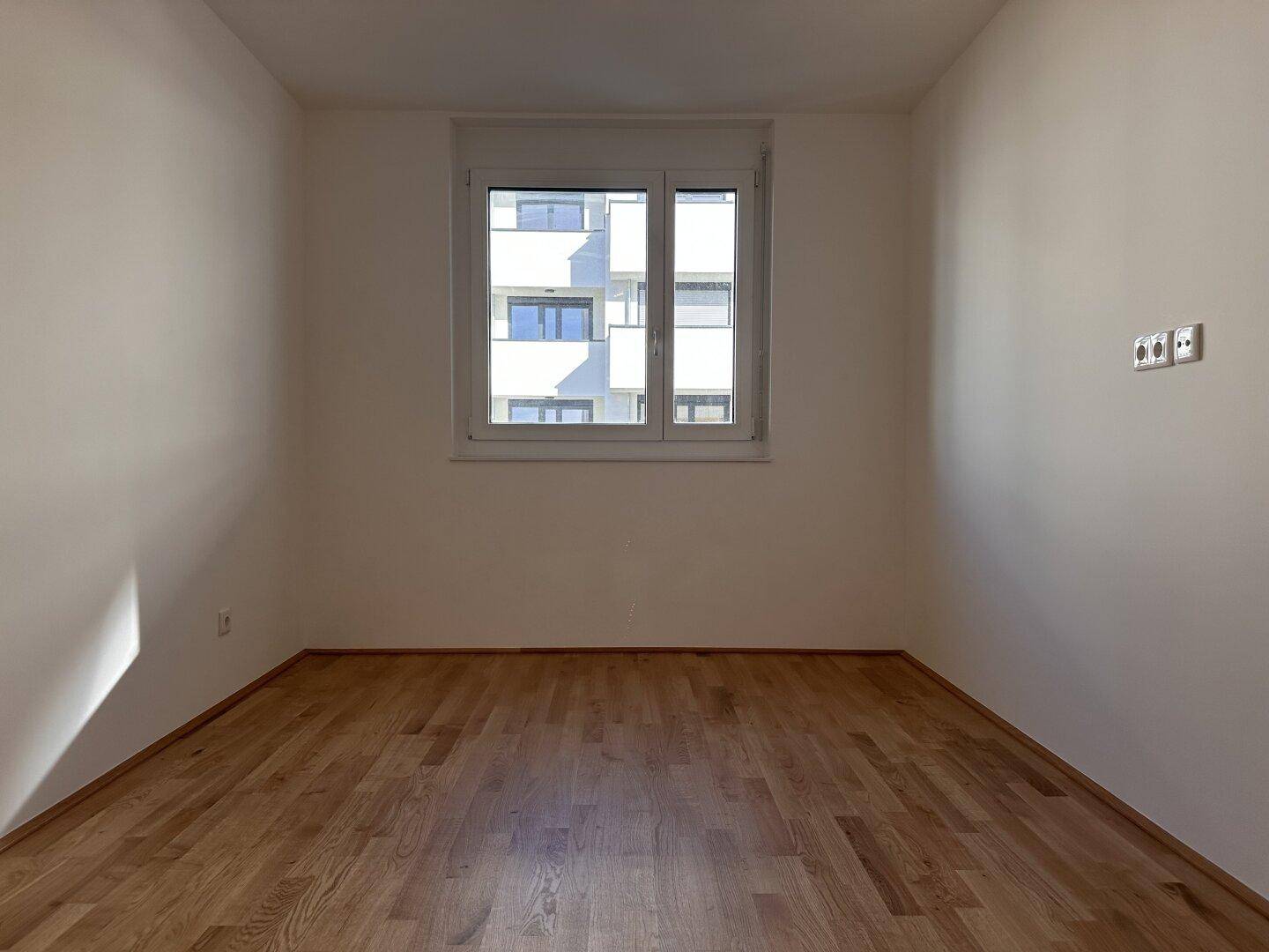 Helles Schlafzimmer mit Parkettboden und einem Fenster, das viel Tageslicht hereinlässt.