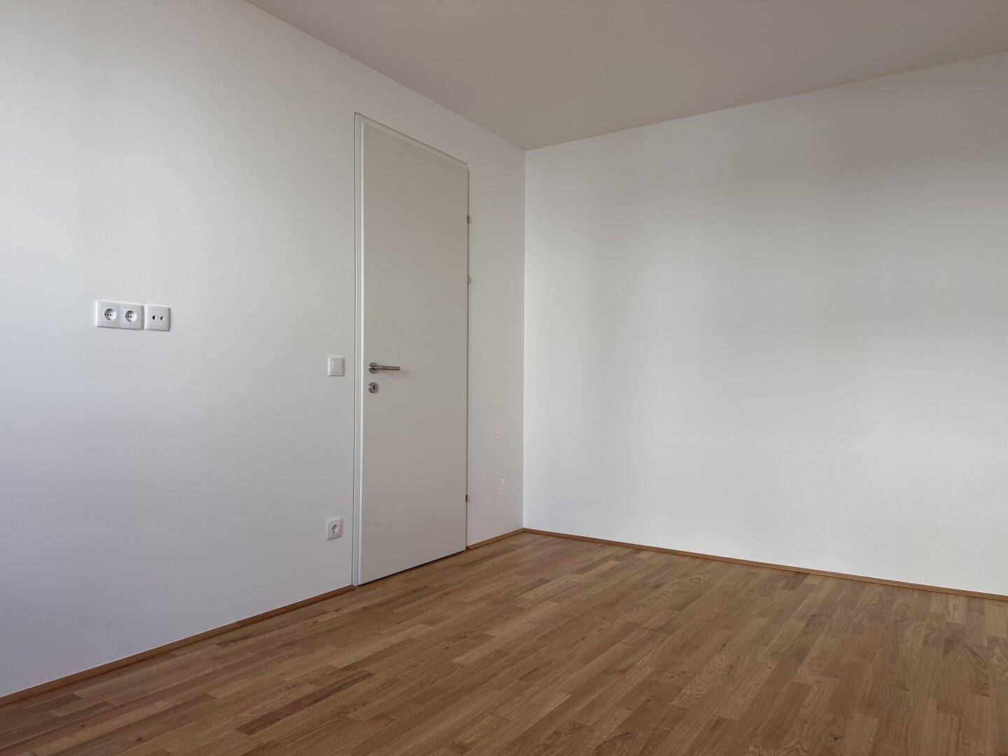 Geräumiges, helles Zimmer mit Parkettboden und einer modernen, bündigen Tür.