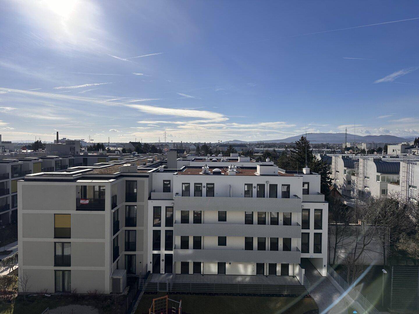 Moderne Wohngebäude unter blauem Himmel, mit Balkonen und einer weiten Aussicht auf die Umgebung.