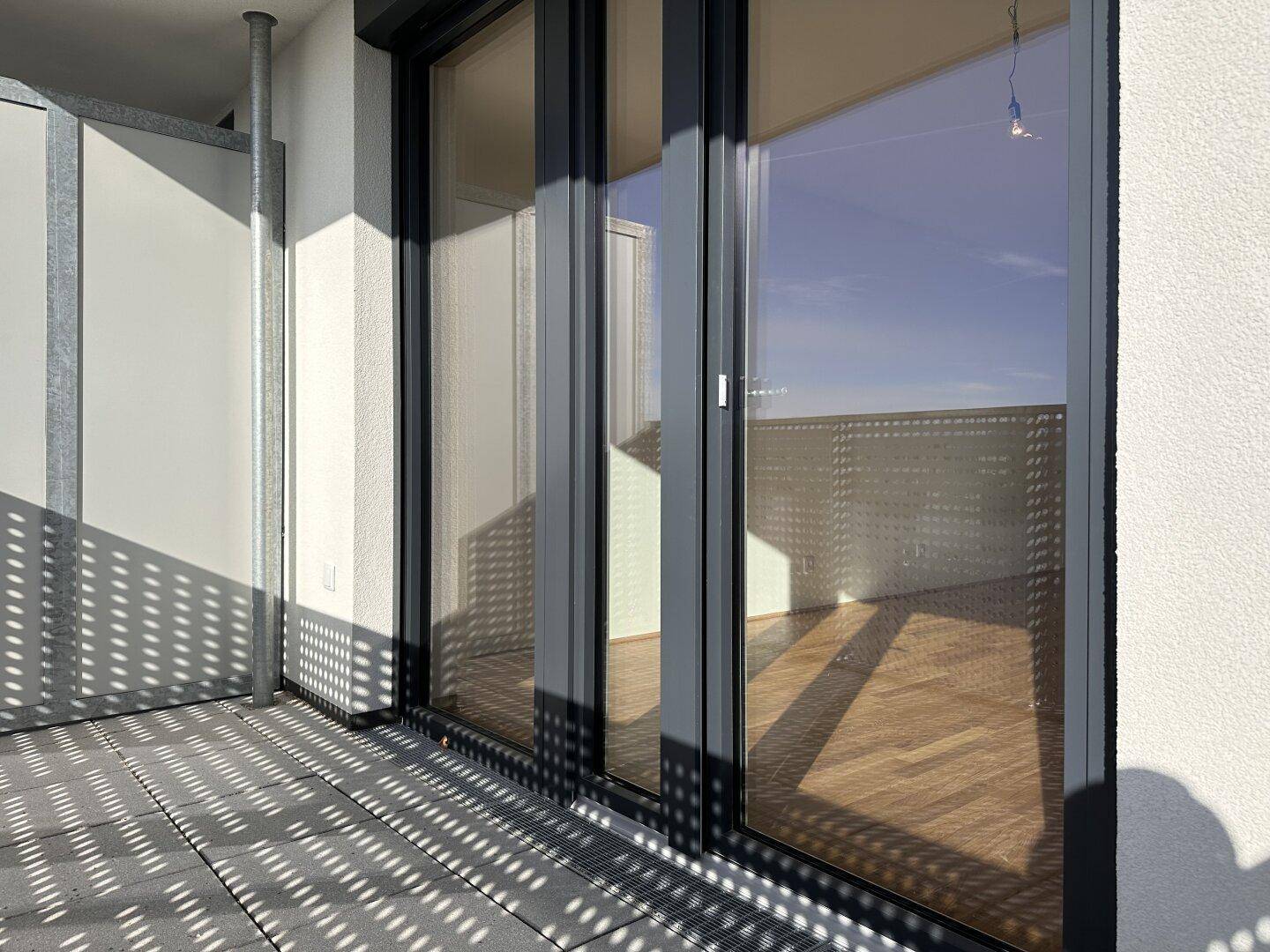 Sonniger Balkon mit großen Fenstern, die das Innere des Raumes widerspiegeln und viel Licht hereinlassen.