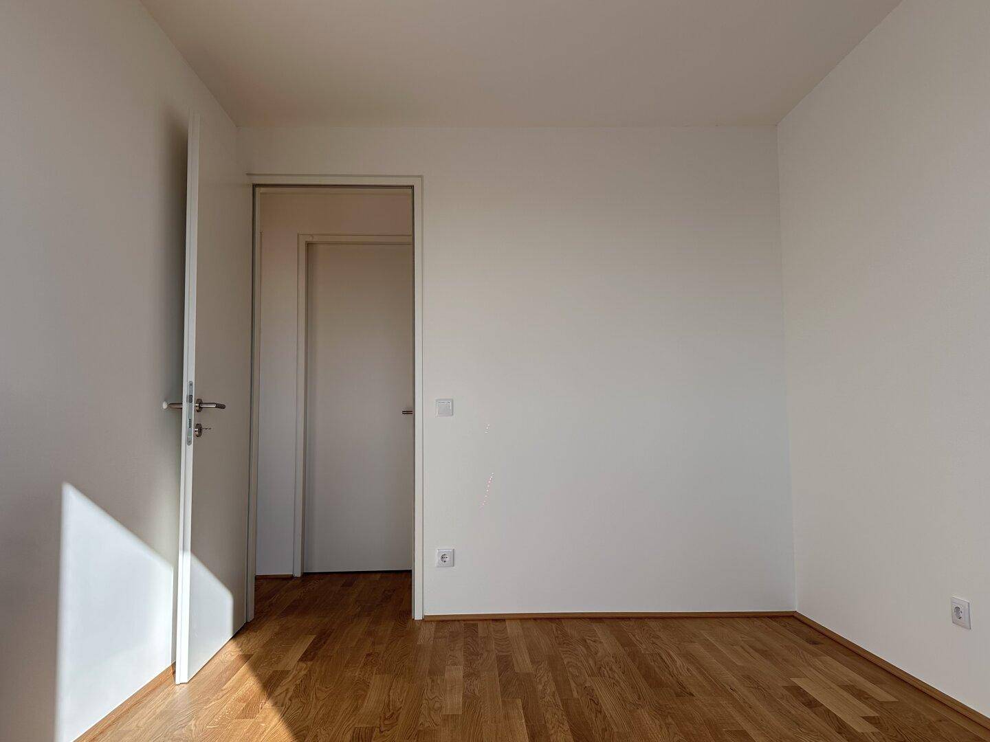 Helles Zimmer mit Holzboden und weißer Tür, das einen sauberen und modernen Eindruck vermittelt.