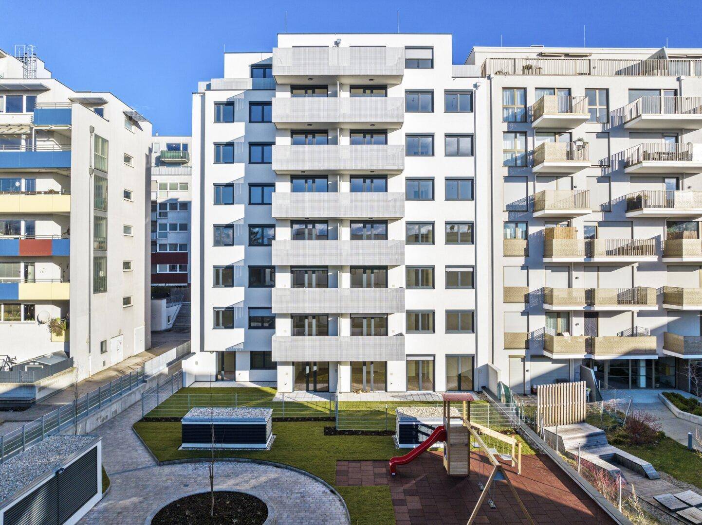 Moderne Wohnanlage mit Gemeinschaftsgarten und Kinderspielplatz im Innenhof.