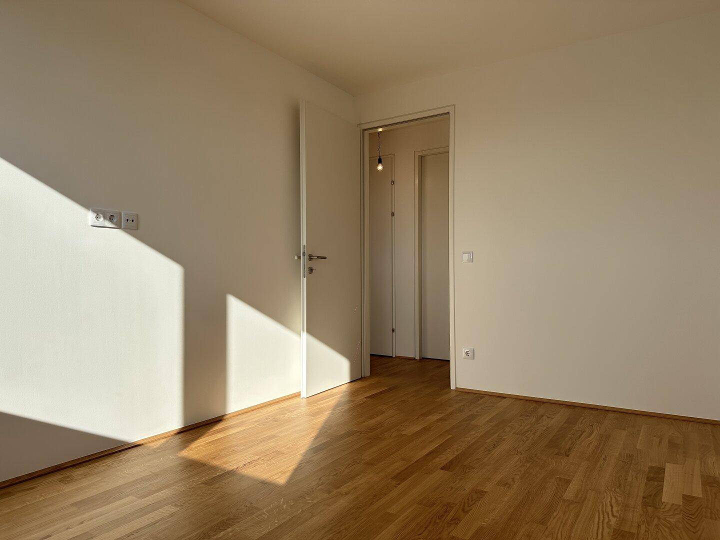 Geräumiges Zimmer mit Parkettboden und Zugang zu einem weiteren Raum, durchflutet von Sonnenlicht.