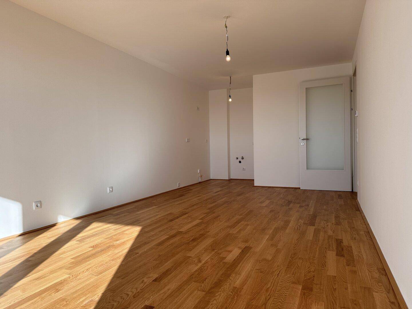 Geräumiges Wohnzimmer mit Parkettboden und einer Tür, die zu weiteren Räumen führt.