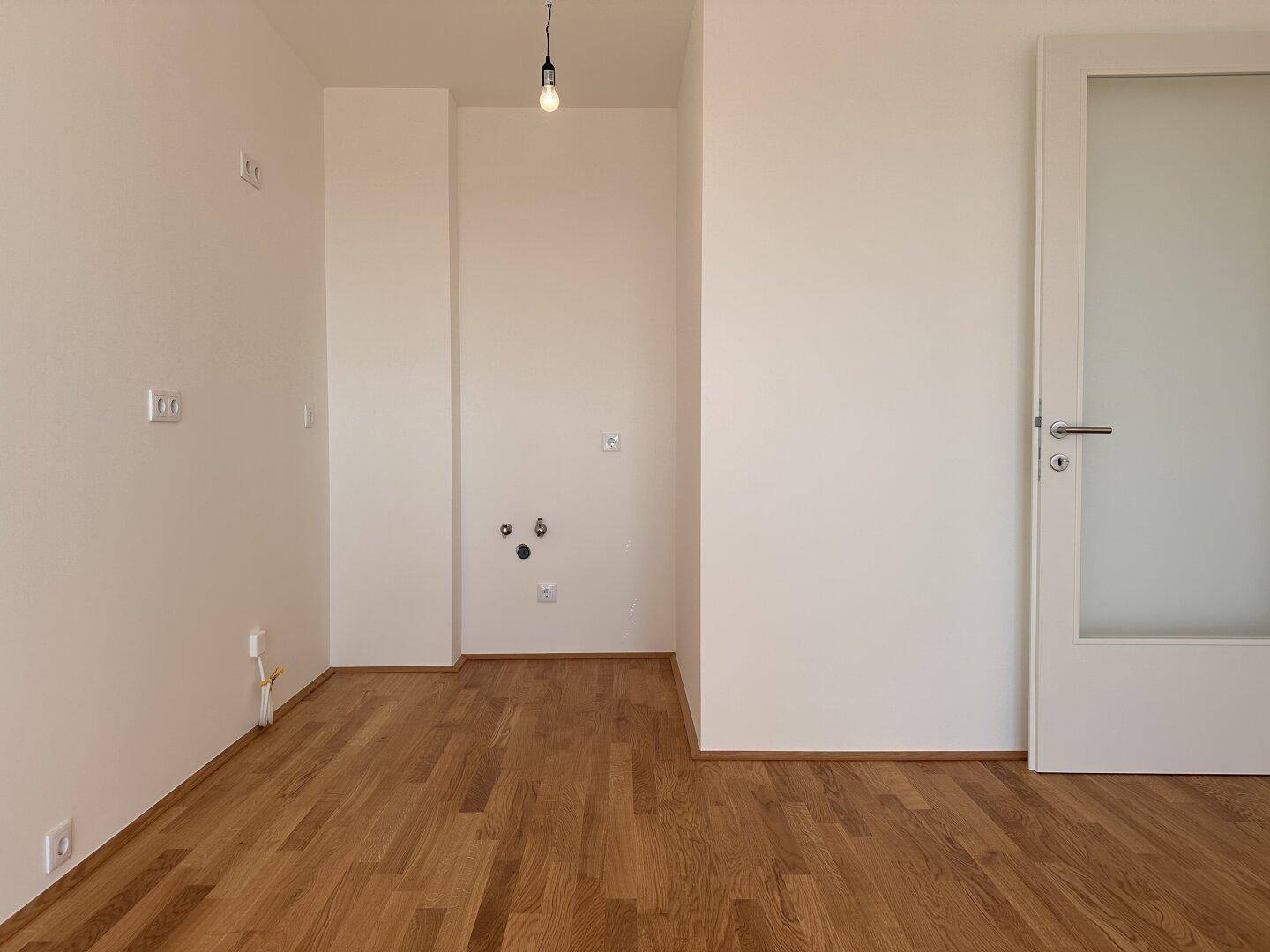 Heller Raum mit Parkettboden und Anschlüssen für eine zukünftige Kücheninstallation.