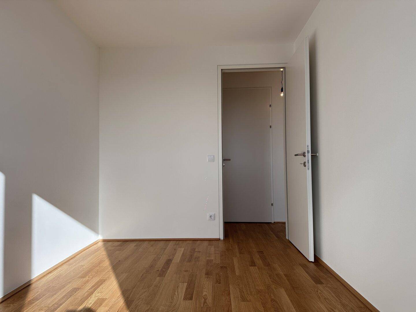 Leeres Schlafzimmer mit Holzboden und weiß gestrichenen Wänden, bereit zur Gestaltung.