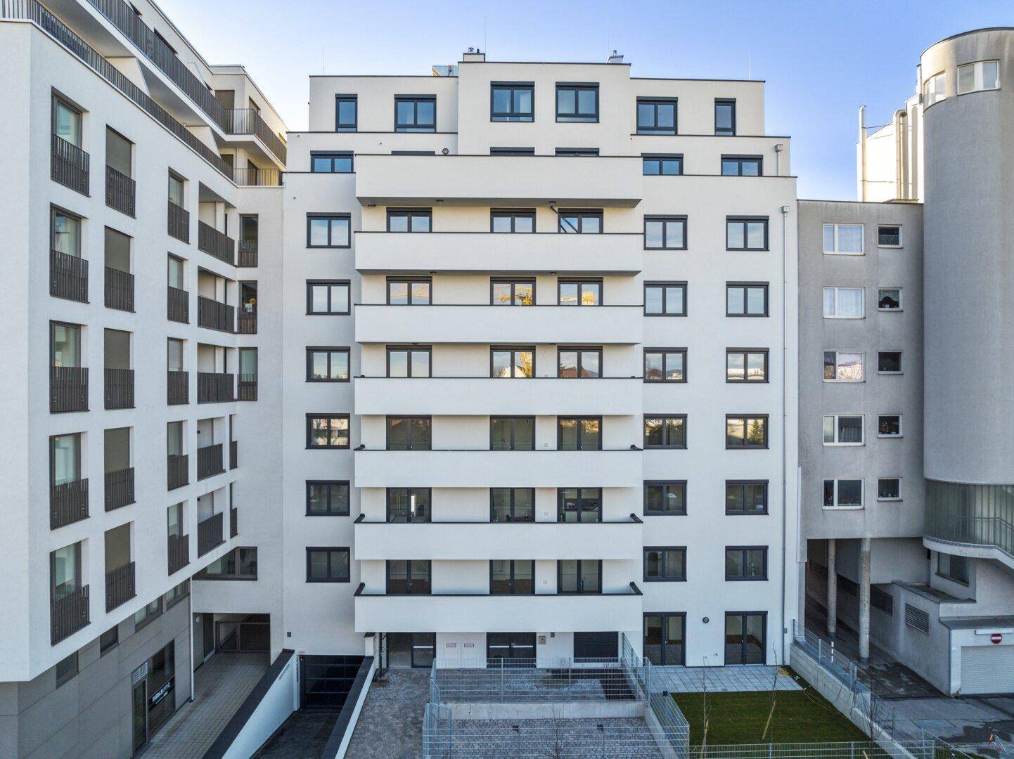 Moderne Wohnhausfassade mit zahlreichen Balkonen und großen Fenstern in einem städtischen Umfeld.