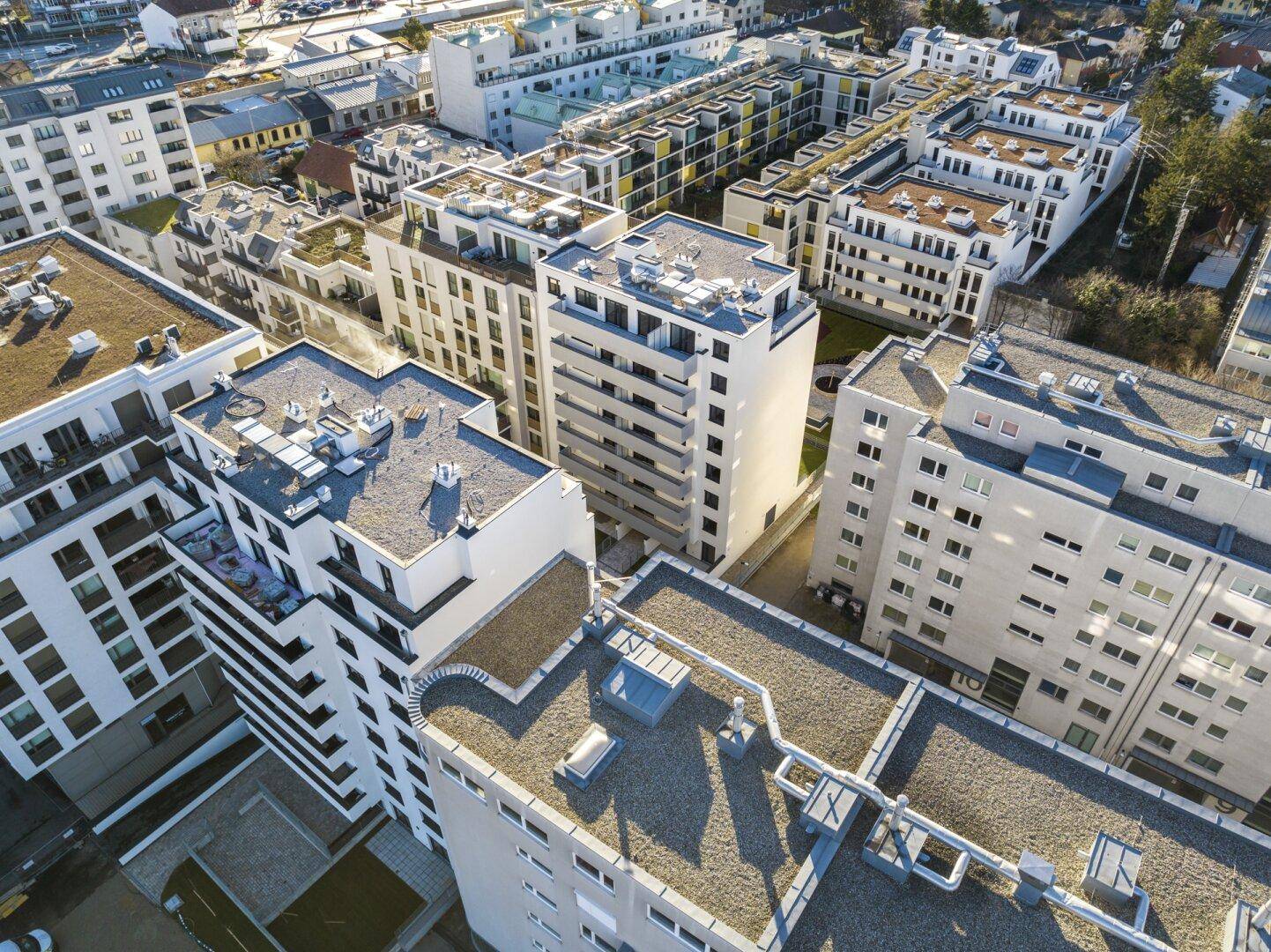 Luftaufnahme eines modernen Wohnkomplexes mit mehreren Gebäuden und Flachdächern in städtischer Umgebung.