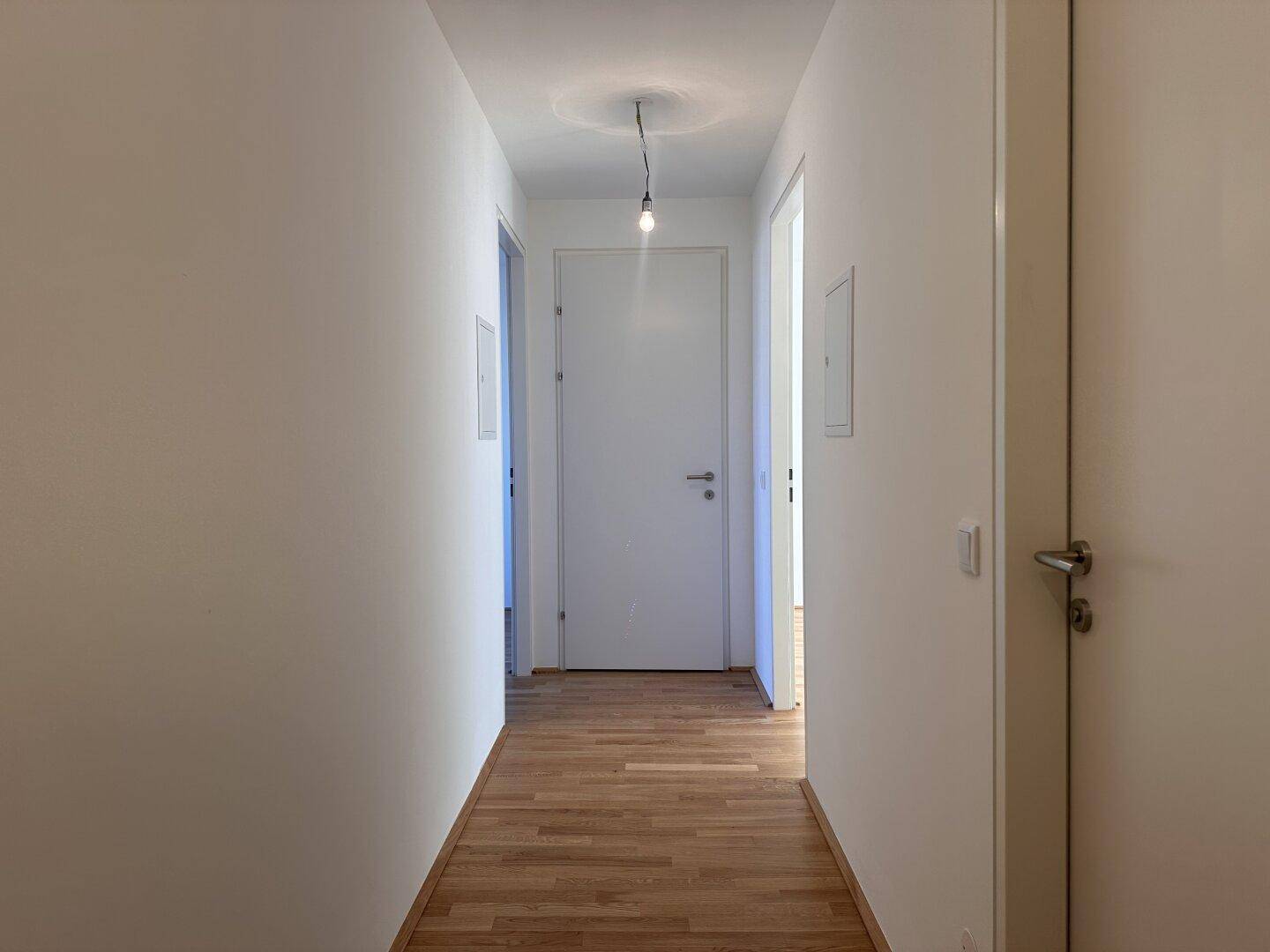 Langer, heller Flur mit Holzboden und mehreren Türen zu den Zimmern.
