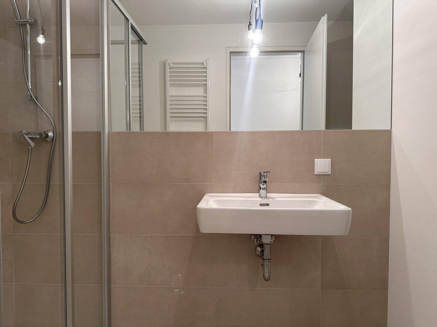 Modernes Badezimmer mit Duschkabine, Waschbecken und großem Spiegel in neutralen Farben.