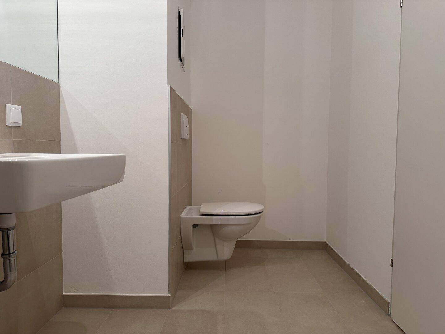 Separate Toilette mit wandhängendem WC und kleinem Waschbecken in modernem Design.