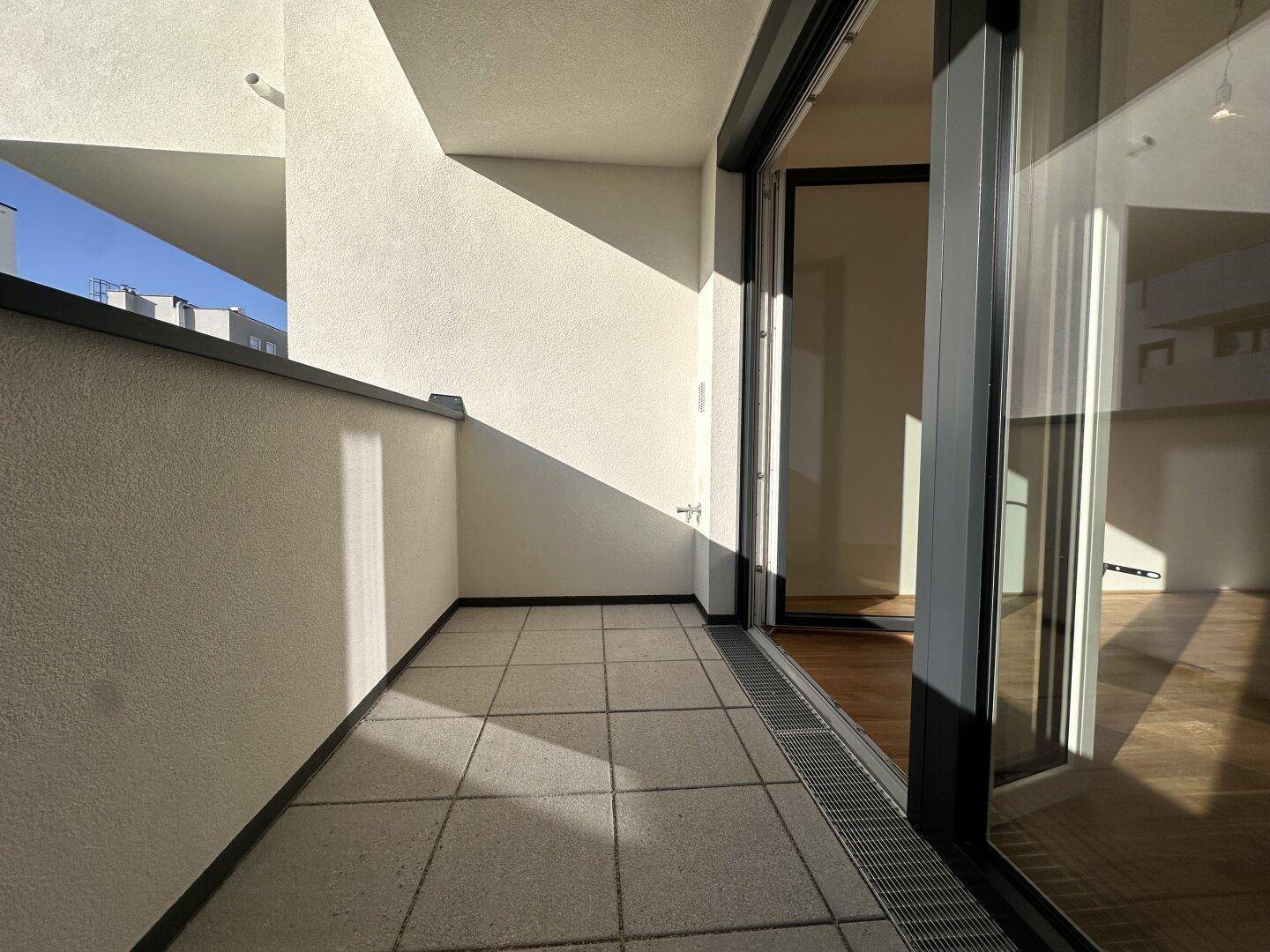 Heller Balkon mit Fliesenboden und Blick auf die umliegenden Gebäude im Innenhof.