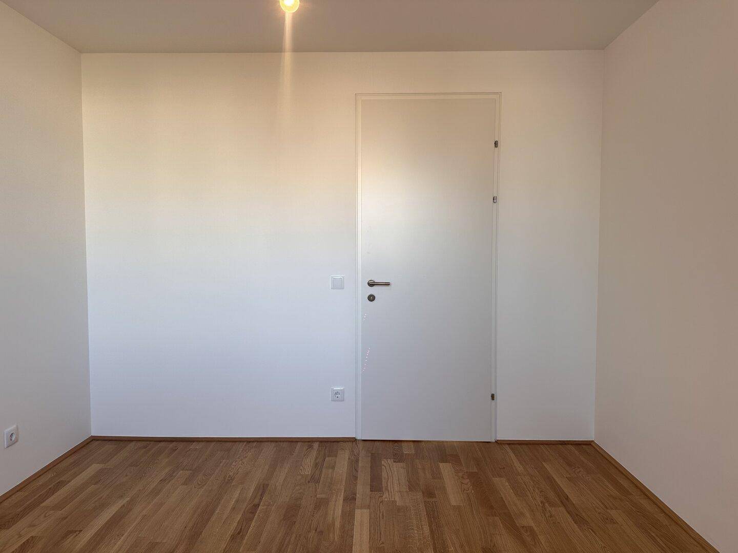 Helles Schlafzimmer mit Holzboden und weiß gestrichenen Wänden, bereit zum Einzug.