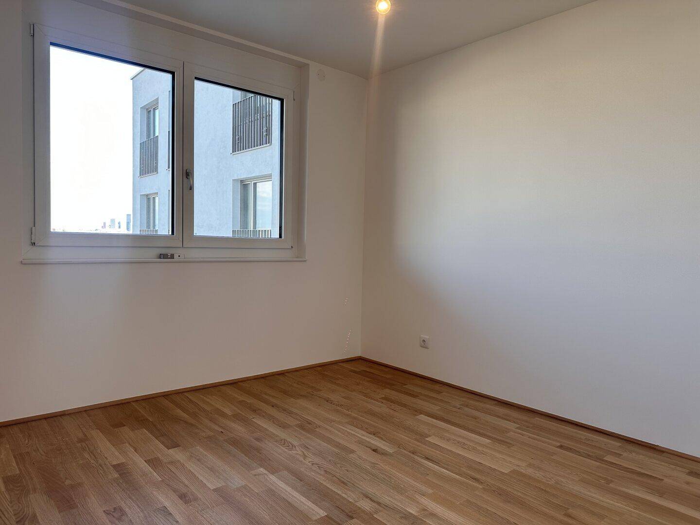 Schlafzimmer mit Holzboden und großem Fenster, das viel Tageslicht hereinlässt.