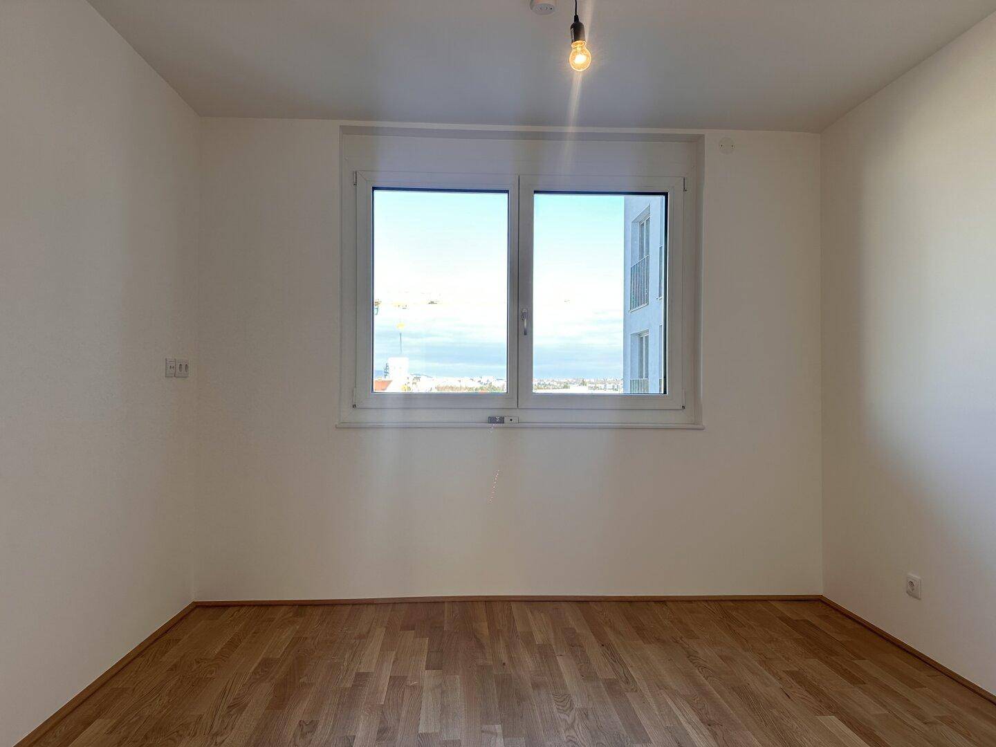 Helles Zimmer mit Holzboden und weitem Blick aus dem Fenster über die Stadt.