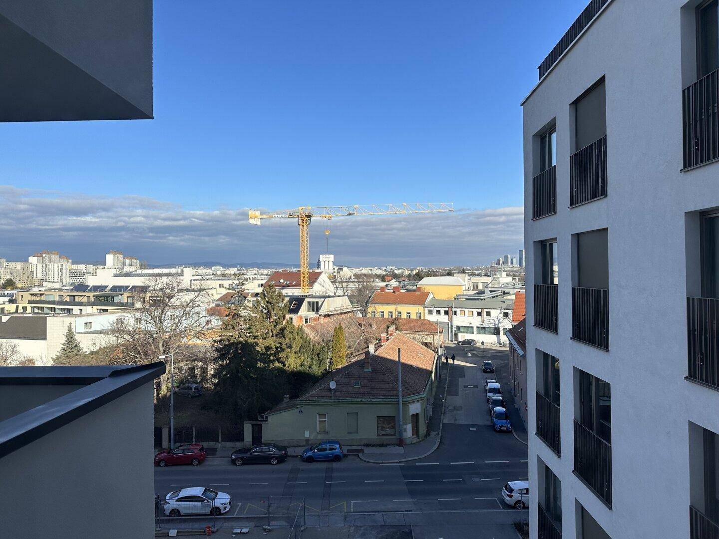 Weitblick über die Stadt mit Gebäuden und einem Baukran unter blauem Himmel.