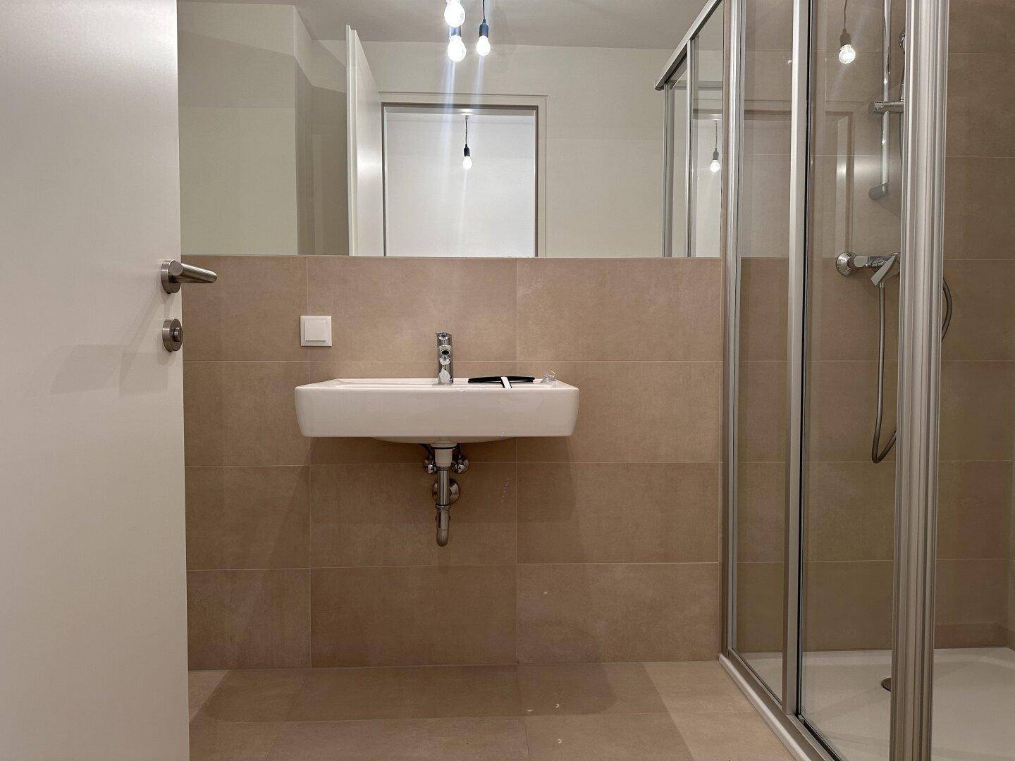 Modernes Badezimmer mit beigefarbenen Fliesen, Einzelwaschbecken und einer Duschkabine.