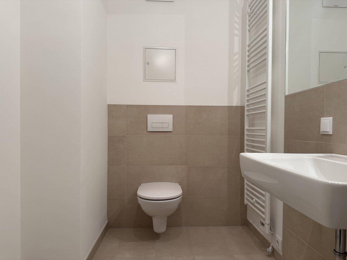 Sauberes WC mit wandhängender Toilette, Einzelwaschbecken und beheiztem Handtuchhalter.