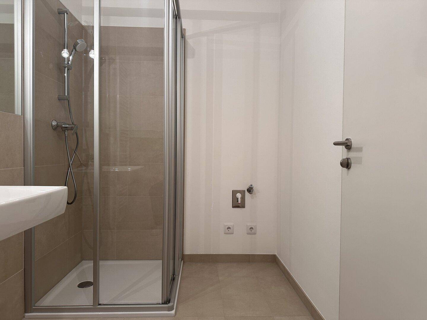 Modernes Badezimmer mit Duschkabine und Anschlüssen für eine Waschmaschine.