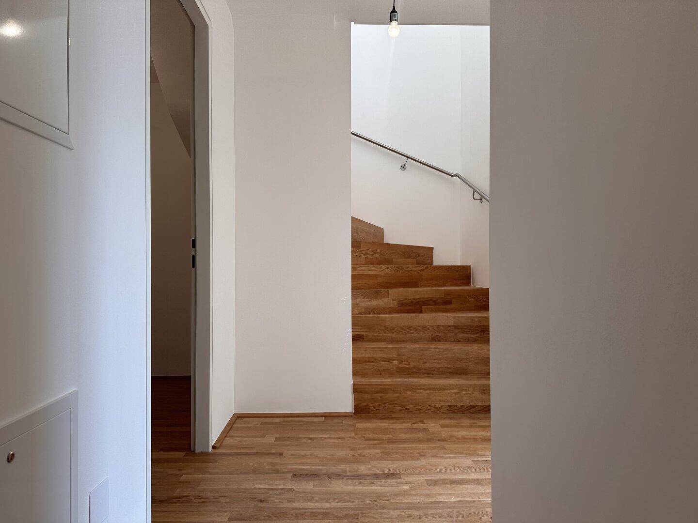 Heller Flur mit Holztreppe und modernem Geländer, verbindet die Wohnebenen.
