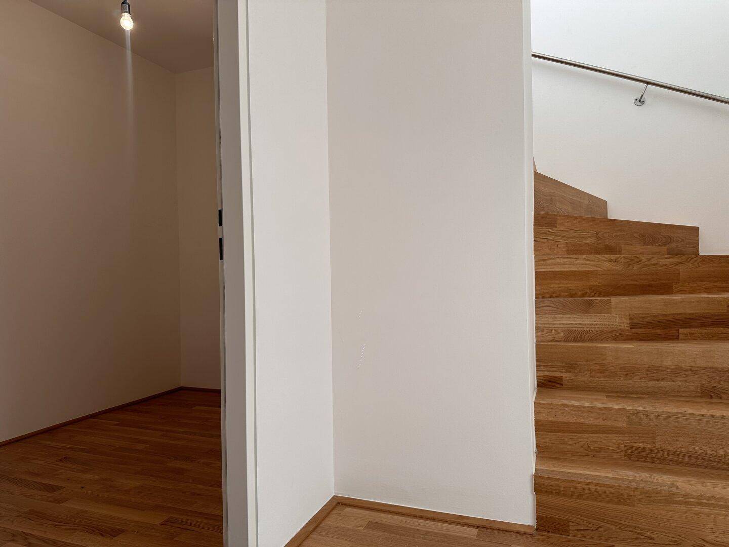 Treppenaufgang mit Holzstufen und schlichtem Handlauf, führt in die obere Etage.