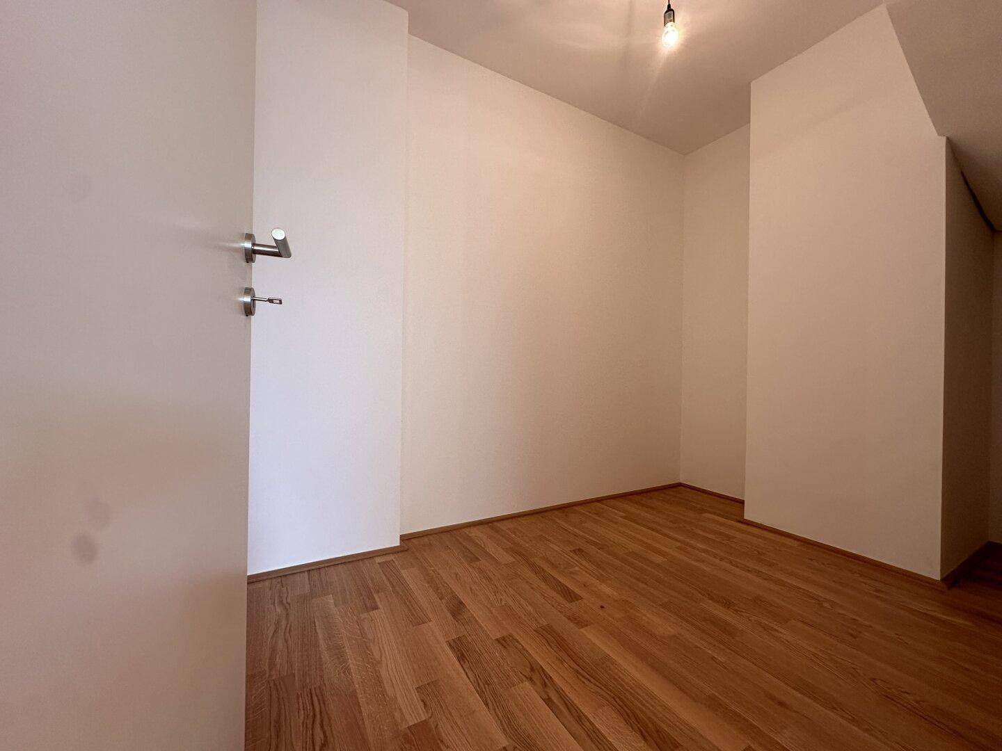 Helles Zimmer mit Parkettboden und weiß gestrichenen Wänden, ideal als Schlaf- oder Arbeitszimmer.