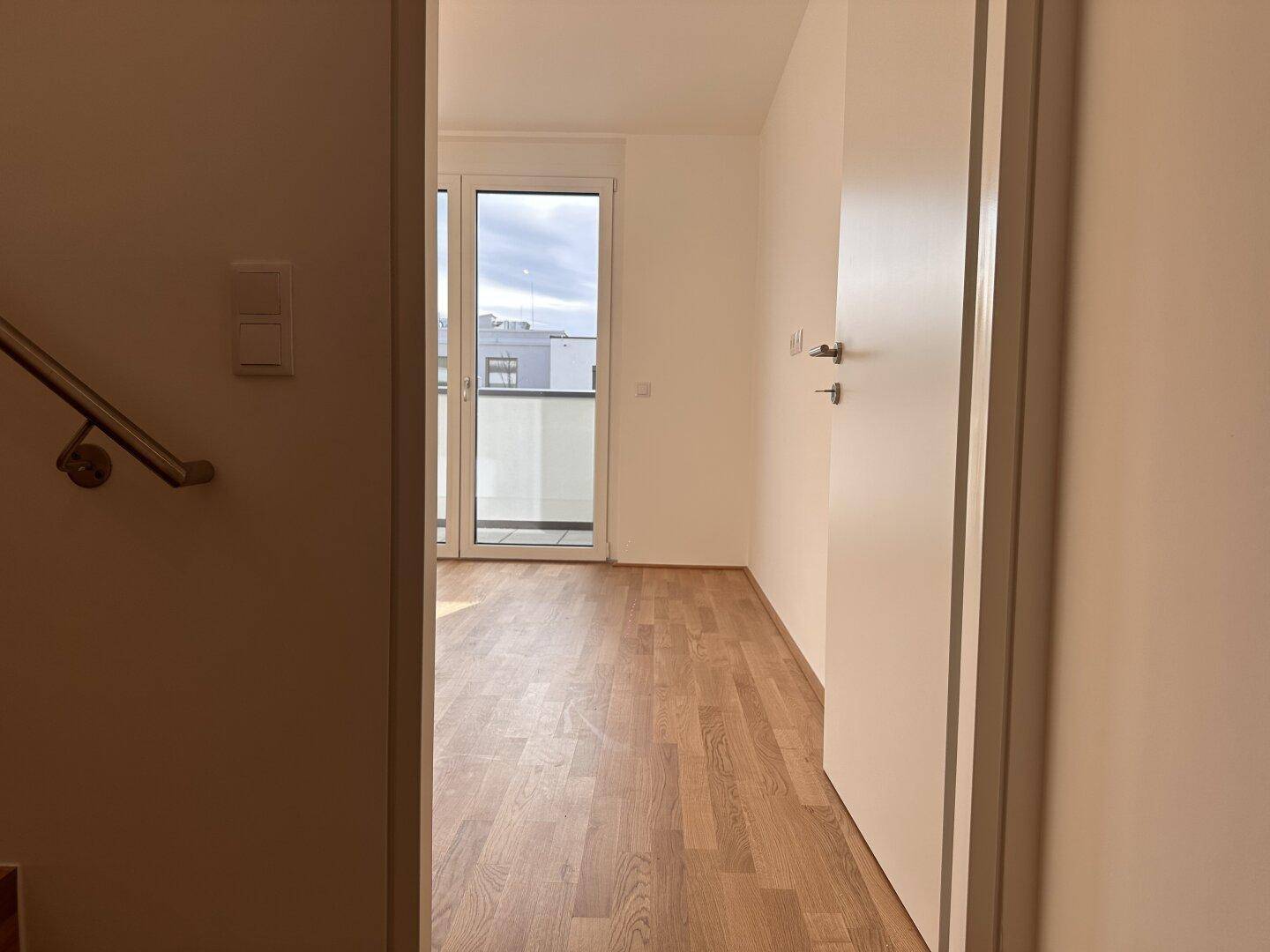 Heller Durchgang zu einem Zimmer mit großen Fenstern und Zugang zu einem Außenbereich.