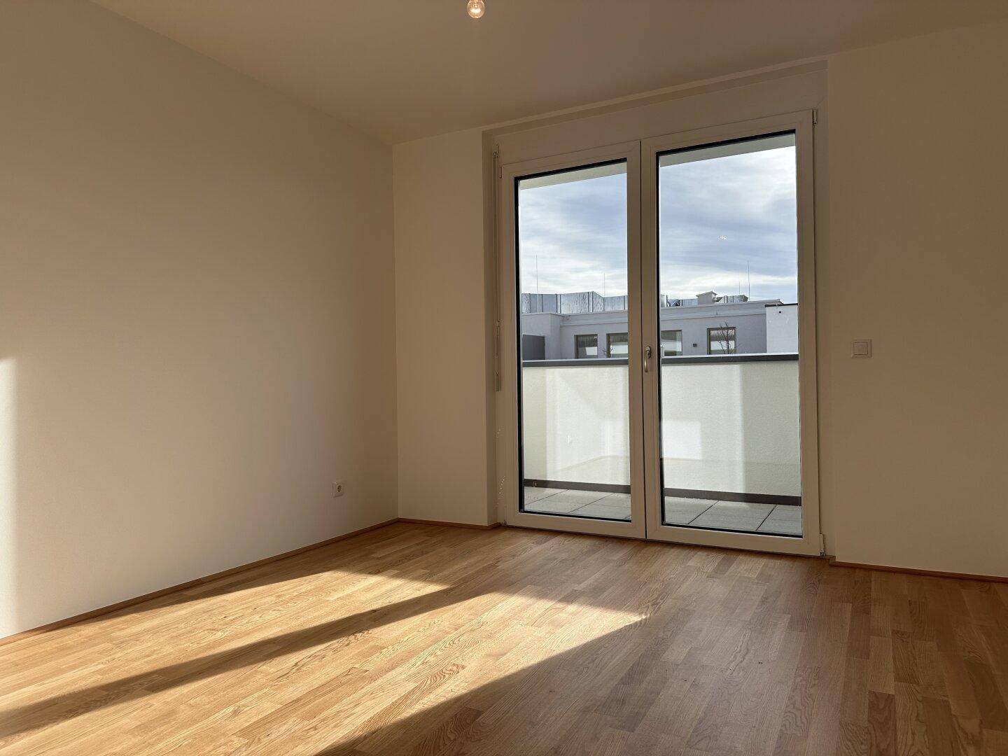 Heller Wohnraum mit Holzboden und großzügigem Balkonzugang, ideal für sonnige Tage.