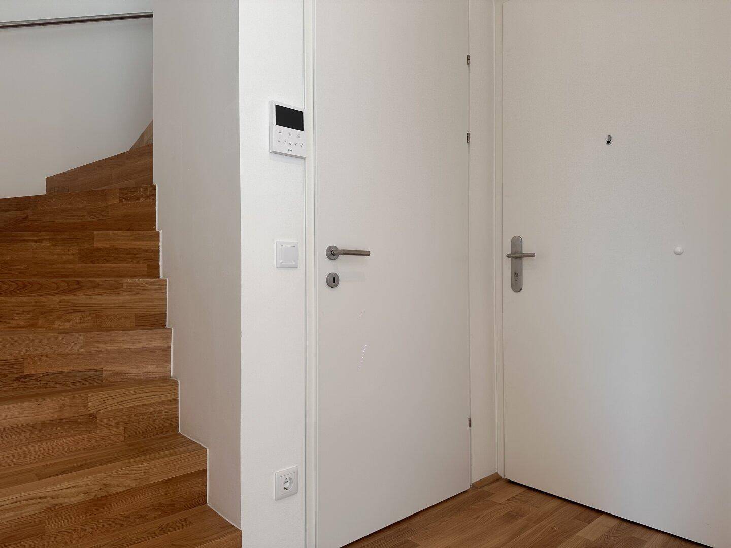 Eingangsbereich mit Holztreppe und Sicherheitssystem an der Wand.