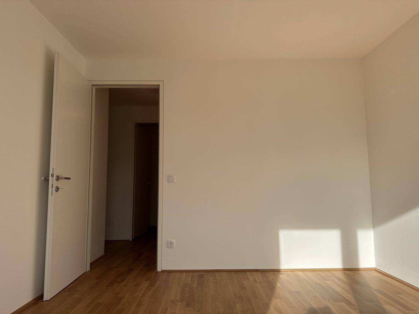 Helles Schlafzimmer mit Holzboden und schlichten Wänden, bietet eine ruhige Atmosphäre.