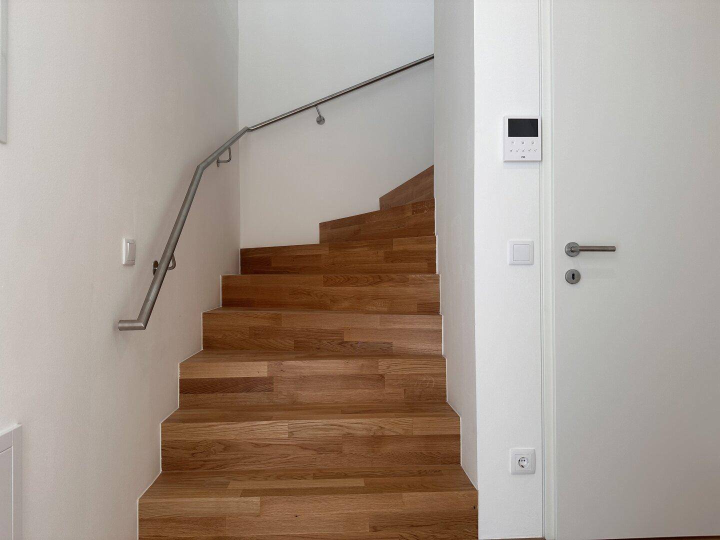 Moderne Holztreppe mit Edelstahlgeländer in einem hellen Treppenhaus.