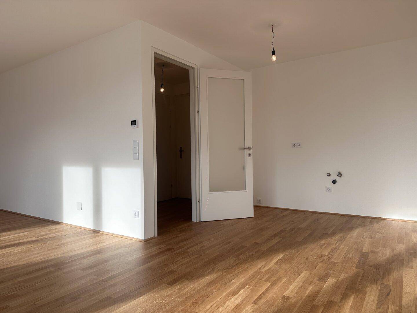 Leerer Raum mit Parkettboden und Anschlüssen für Wasser und Strom, ideal als Hauswirtschaftsraum.