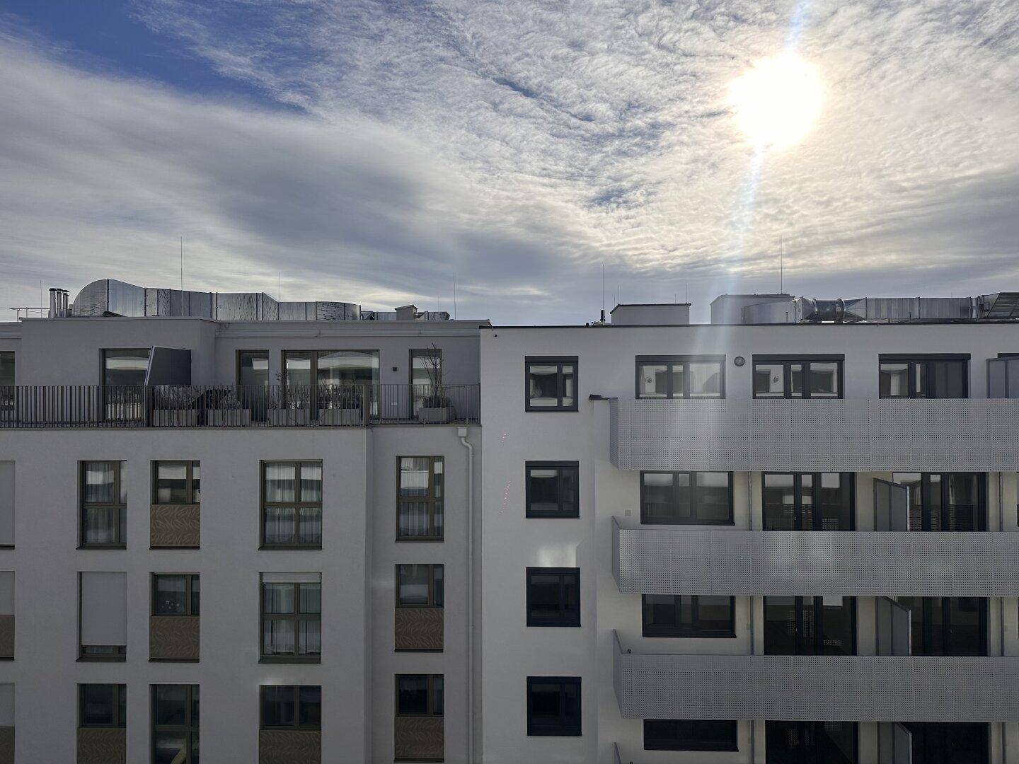 Blick auf die moderne Gebäudefassade und die umliegenden Dächer unter einem weiten Himmel.