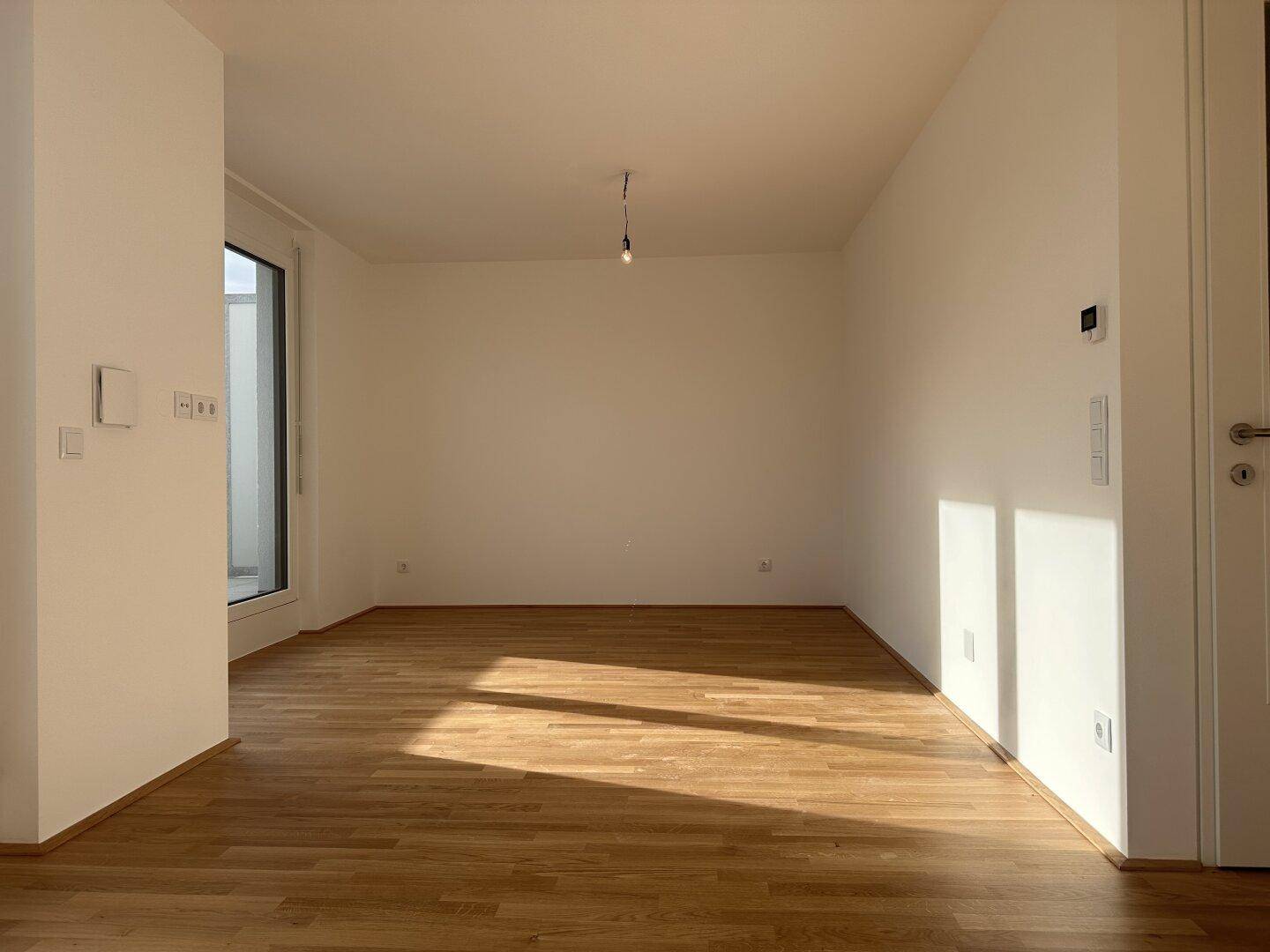 Leerer Raum mit Parkettboden und viel Tageslicht, ideal für verschiedene Nutzungsmöglichkeiten.
