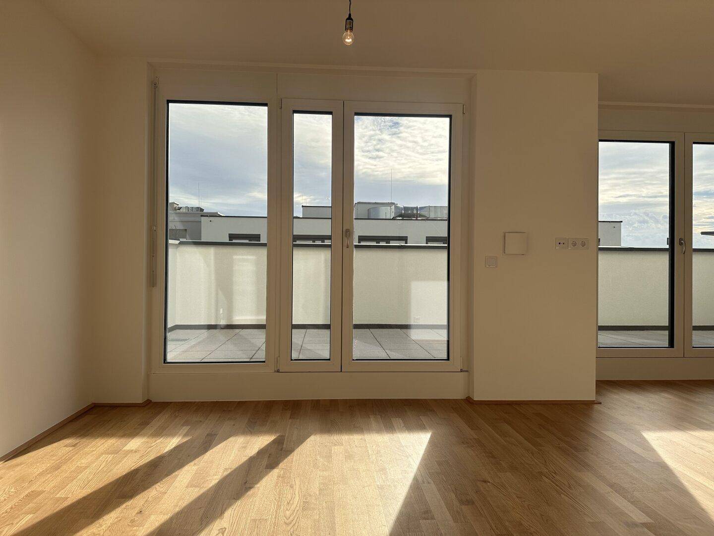 Helles Zimmer mit Parkettboden und großen Fenstern, die Zugang zu einer Terrasse bieten.