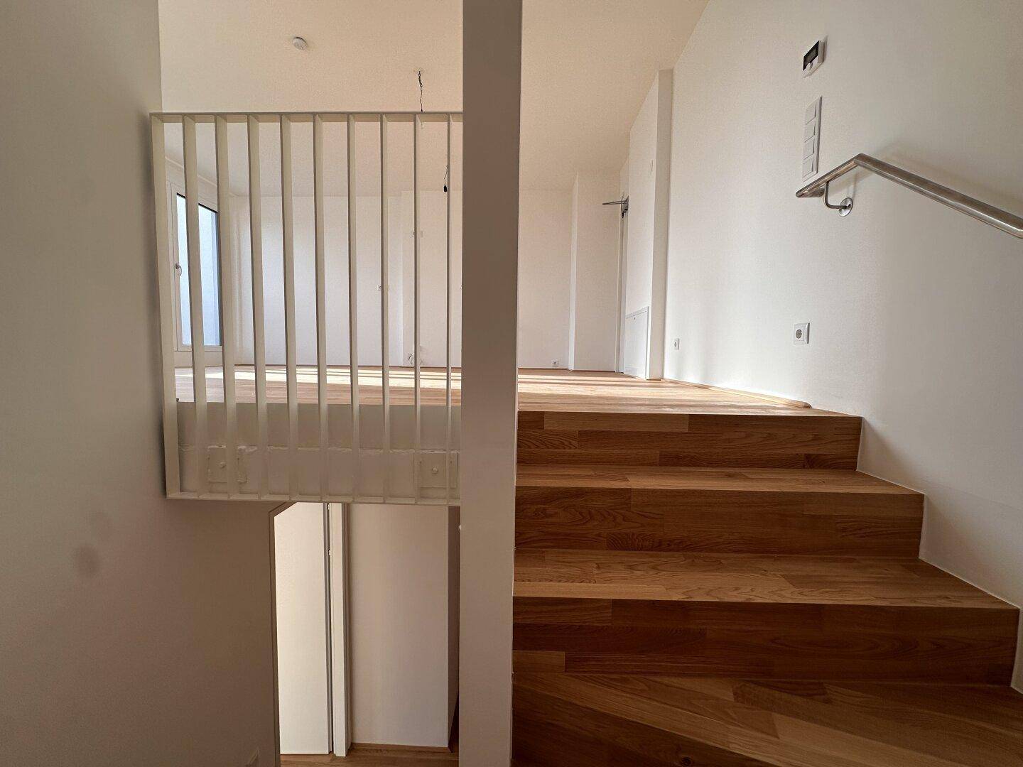 Offener Wohnbereich mit Holztreppe und Galerie, die verschiedene Ebenen verbindet.