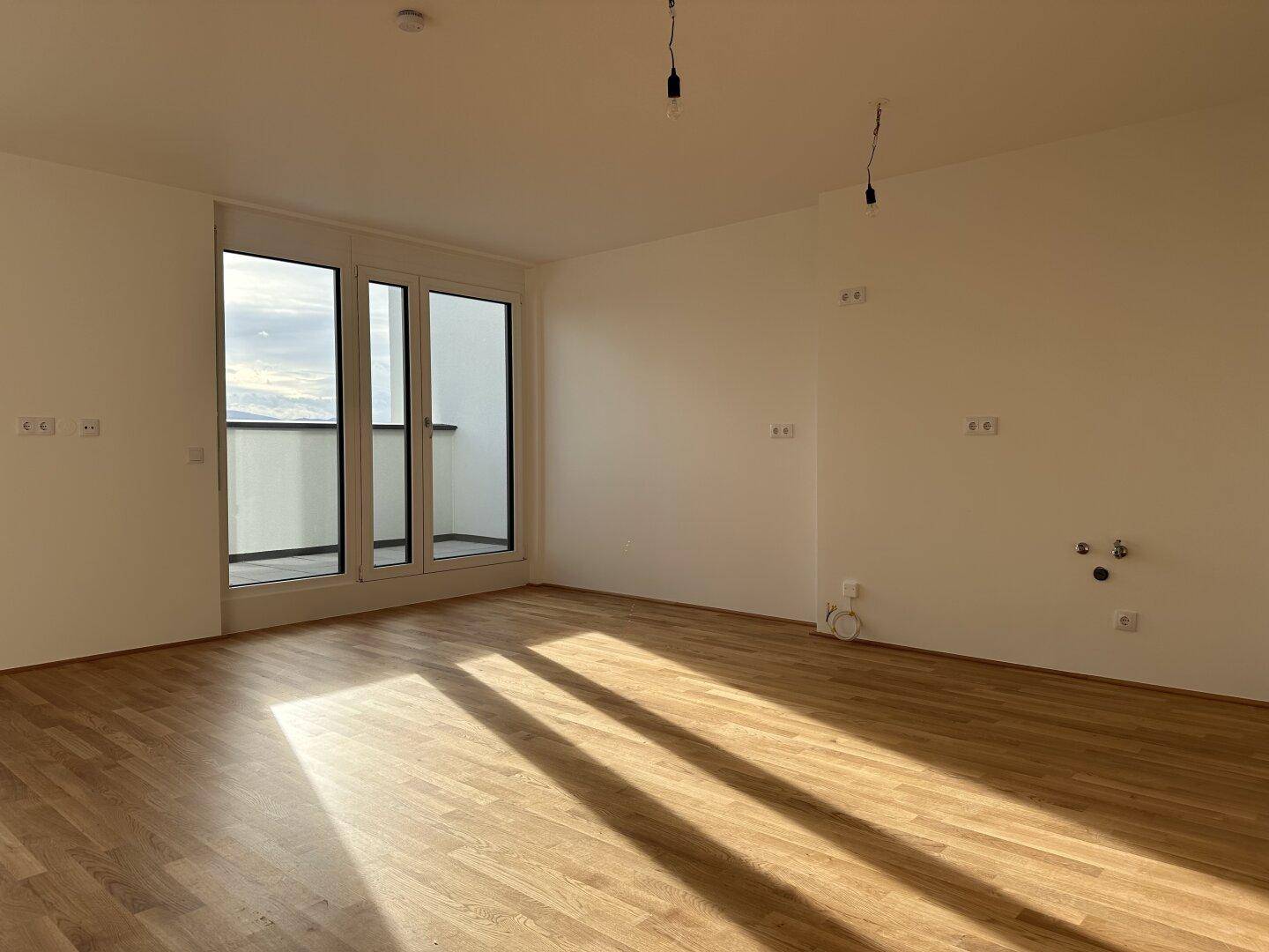Geräumiger Wohnbereich mit Parkettboden und großen Fenstern, die viel Sonnenlicht hereinlassen.