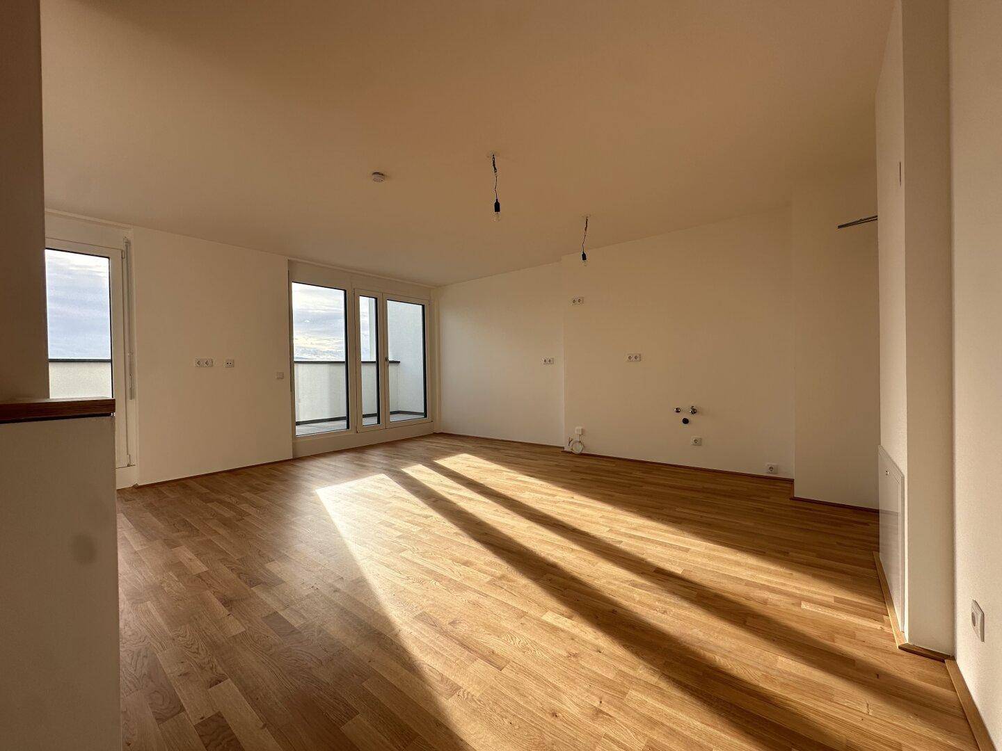 Weitläufiger, heller Wohnbereich mit Parkettboden und Zugang zu einem Balkon, ideal für offenes Wohnen.