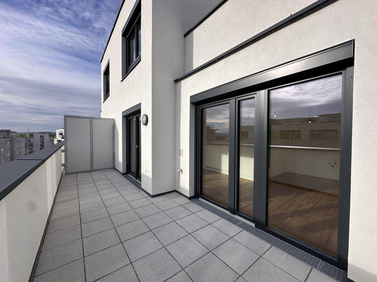 Große, geflieste Terrasse mit Schiebetüren zum Innenbereich und moderner Architektur.