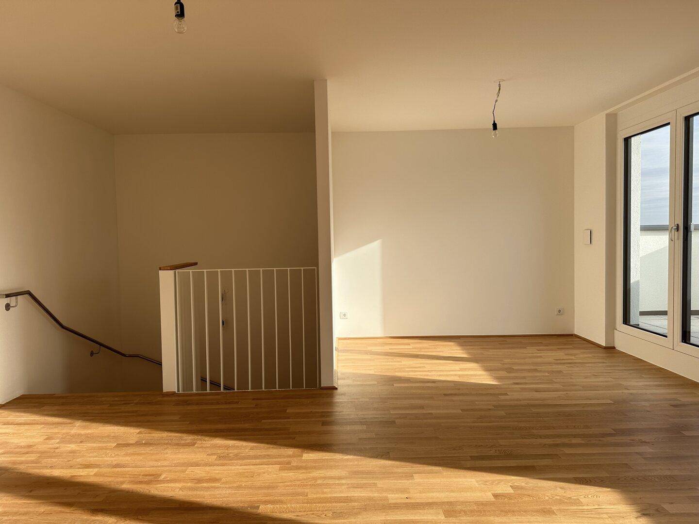 Geräumiger Wohnbereich mit Parkettboden und Treppenaufgang, durchflutet von natürlichem Licht.