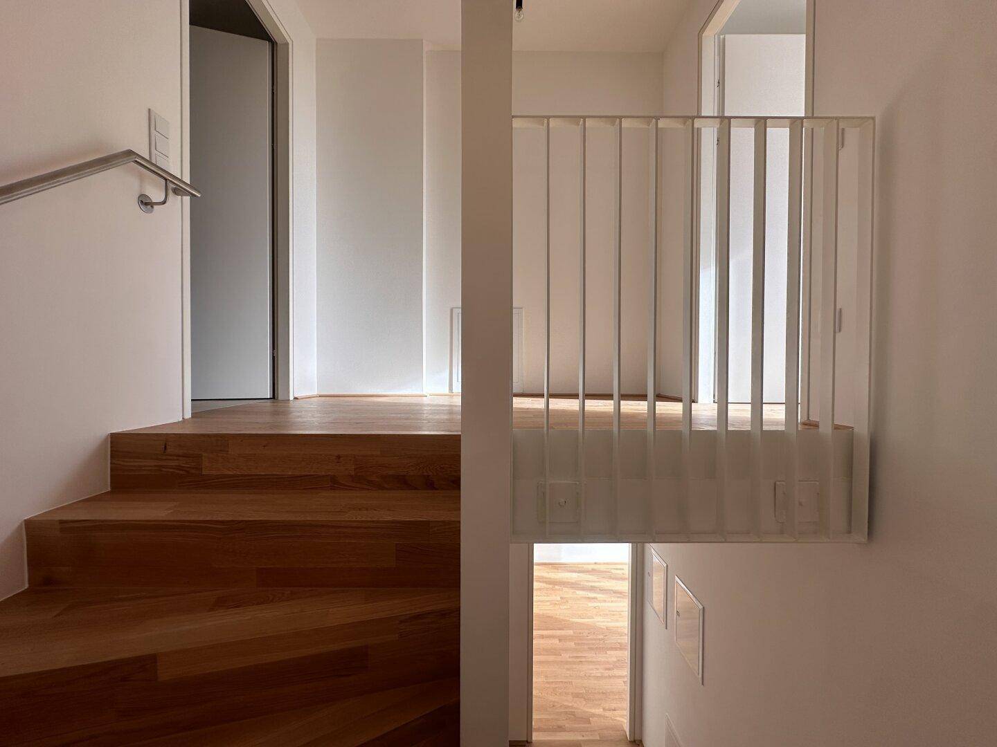 Treppenhaus mit Holzstufen und modernem Geländer, das zu einem oberen Flur führt.