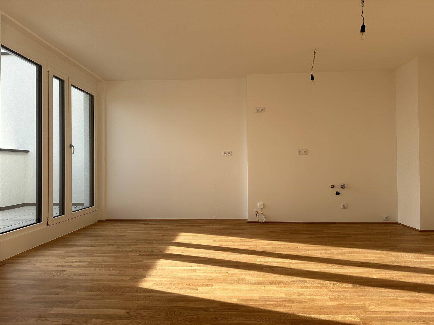 Heller Wohnbereich mit Parkettboden und großen Fenstern, die den Raum mit Sonnenlicht füllen.