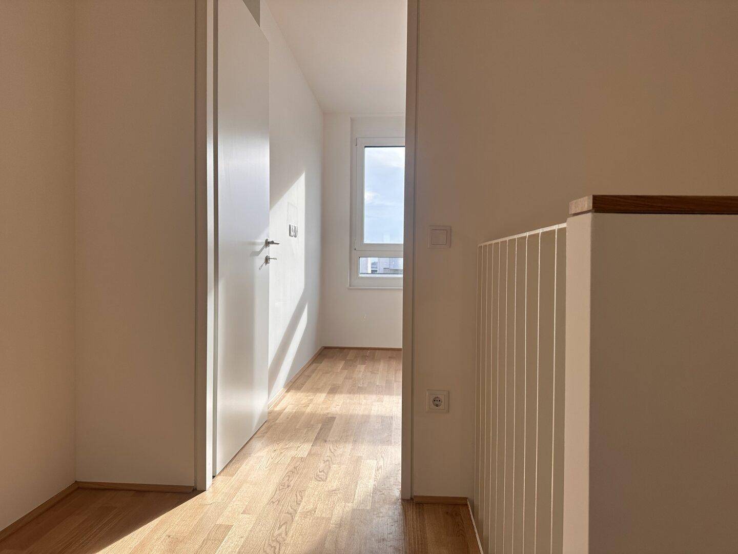 Heller Flur mit Parkettboden, der zu einem Zimmer mit Fenster führt.
