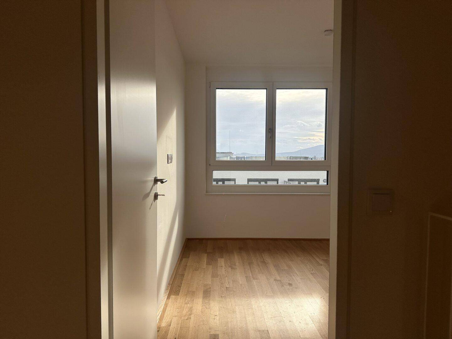 Helles Schlafzimmer mit Parkettboden und großem Fenster, das viel Tageslicht bietet.