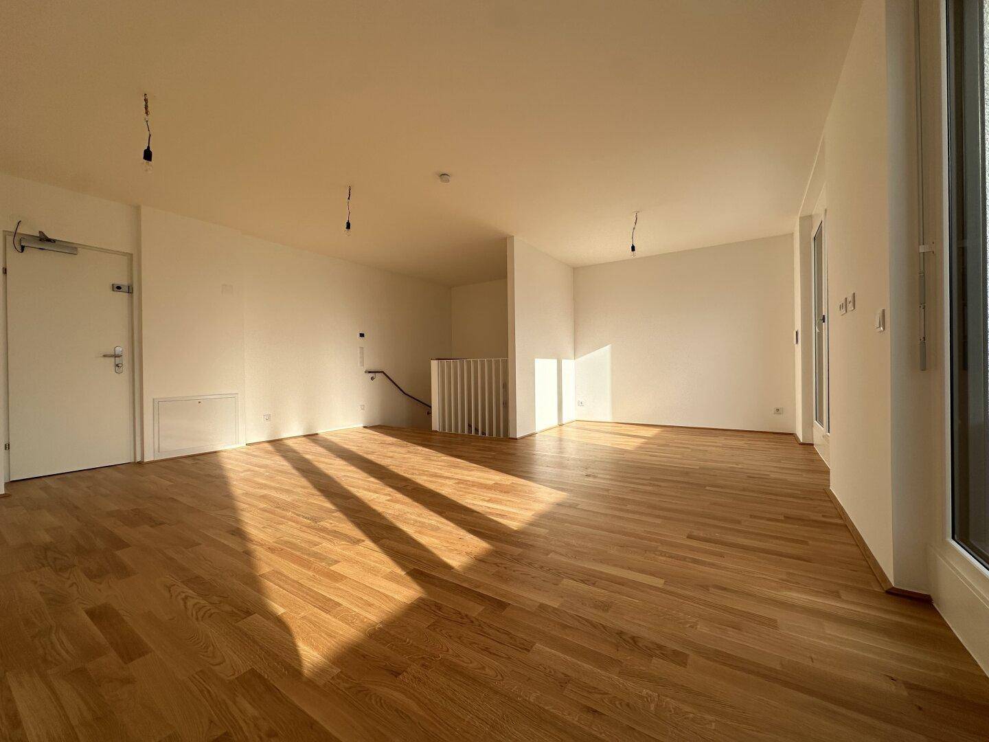 Geräumiger, heller Wohnbereich mit Parkettboden und Zugang zu einem Balkon, durchflutet von Sonnenlicht.