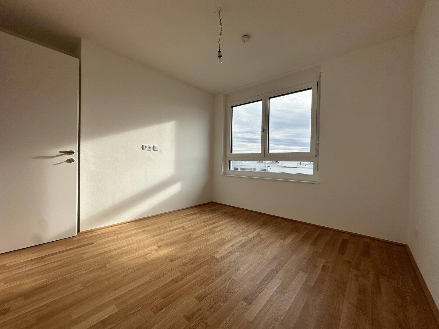 Modernes Schlafzimmer mit Parkettboden und großem Fenster, das für eine helle Atmosphäre sorgt.