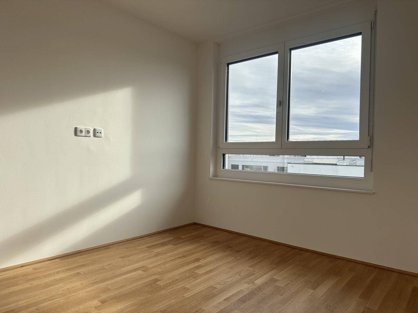 Helles Zimmer mit Parkettboden und Fenster, das viel Sonnenlicht in den Raum lässt.