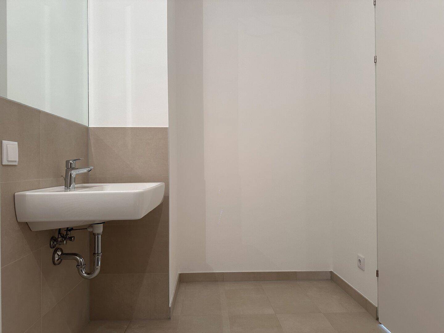 Modernes Badezimmer mit Waschbecken, Spiegel und beigefarbenen Fliesen.